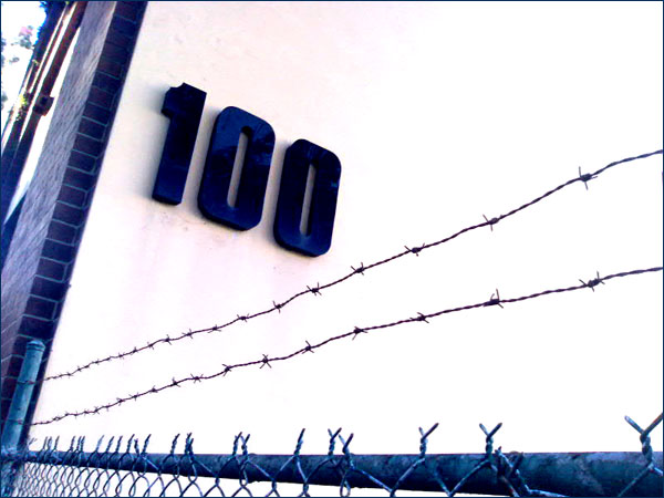 Photograph of a street number, 100, with barbed wire