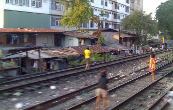 Photograph of girls playing on the railway in Bangkok, with the slum in the background