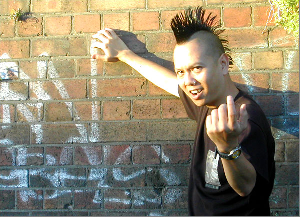Photograph of Trinn Suwannapha with long mohawk, giving the finger