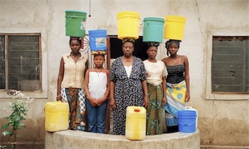 Photograph of Tanzanian women with brightly-coloured plastic water containers balanced on their heads