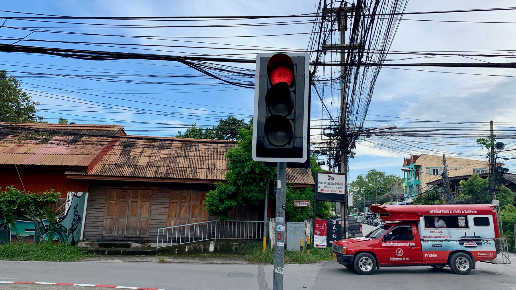 A traffic light at the corner of Thanon Ratmakka and Soi Sam Lan in Chiang Mai's Old City, with a passing Songthaew, the red passenger trucks that form the core of the city's public transport.