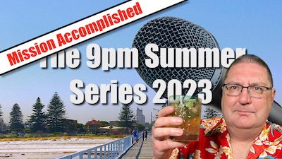 Stilgherrian wears a bright red summer shirt and holds aloft a random brown drink. In the background is a generic beach scene, in fact Largs Bay Pier in Adelaide. The text reads "MISSION ACCOMPLISHED: The 9pm Summer Series 2023".