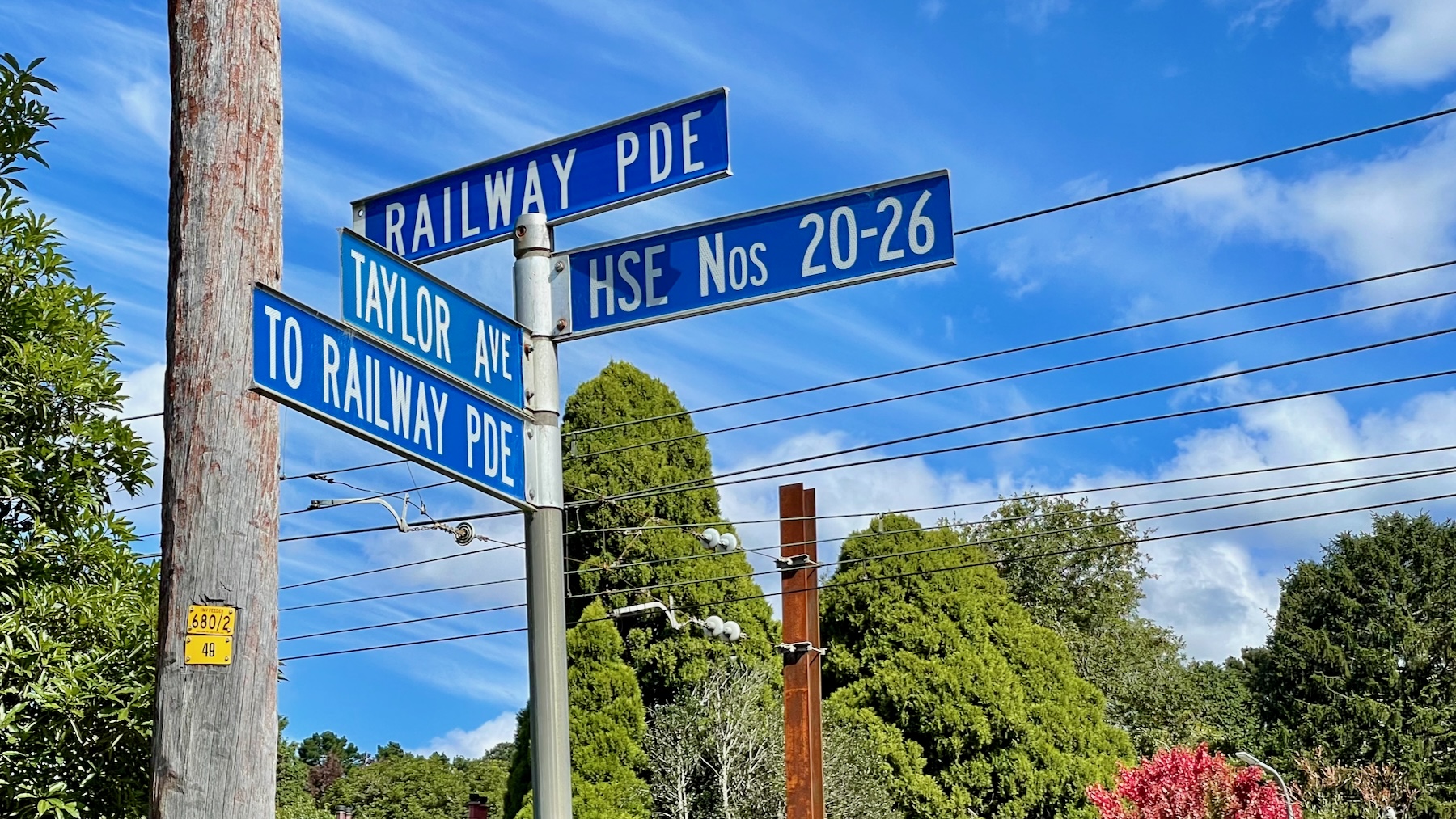 A steel post with street signs. Across the back one reads RAILWAY PDE. Below that, pointing to the right, HSE NOS 20-26. Below that, at 90 degrees to those two, are two more, reading TAYLOR AVE and TO RAILWAY PDE.