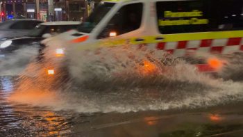 A photo taken at night. An ambulance surges through water, with spray coming up a metre along its side.