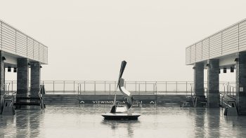 Looking across a rain-soaked concrete plaza to an abstract stainless steel sculpture, then a step up to a railing labelled VIEWING PLATFORM. Beyond that, nothing but a pale grey void, because we're inside a cloud.