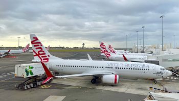 The view down a rank of Boeing 737-800 aircraft, all in white and red Virgin Australia livery, their noses to the right lined up with the terminal's aerobridges.