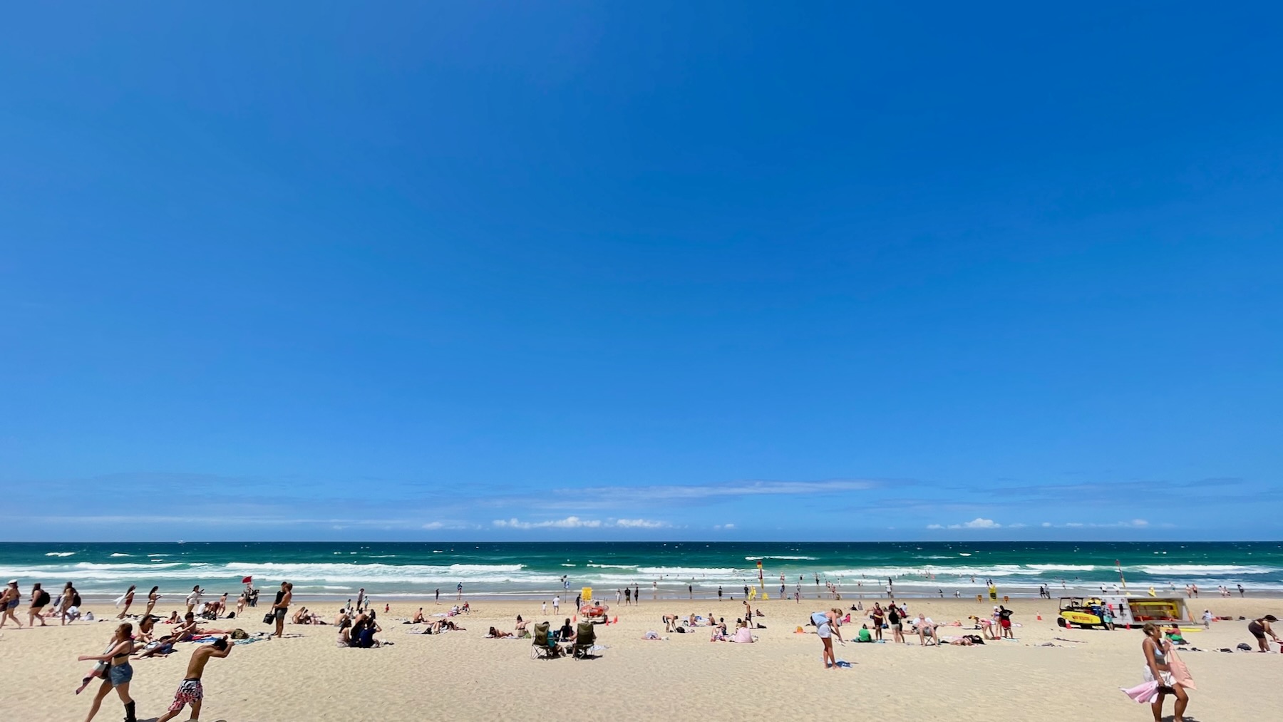 Wide view across off-white sand, past sunbathers and soon-to-be swimmers, to the gently rolling waves of the Pacific Ocean. But the vast majority of the age is the sky, and apart from a line of cloud out bye the horizon, it's a clear and brilliant blue.