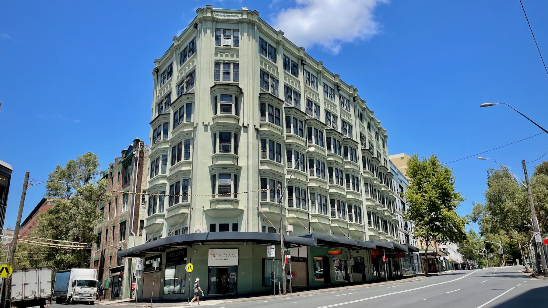 A six-storey art deco building, with a commercial ground floor, two floors of offices with bay windows, and two floors of residential apartments. It's painted an unassuming olive green, and kinda needs repainting again soon. It's a bright sunny day, and the streets around it are almost deserted.