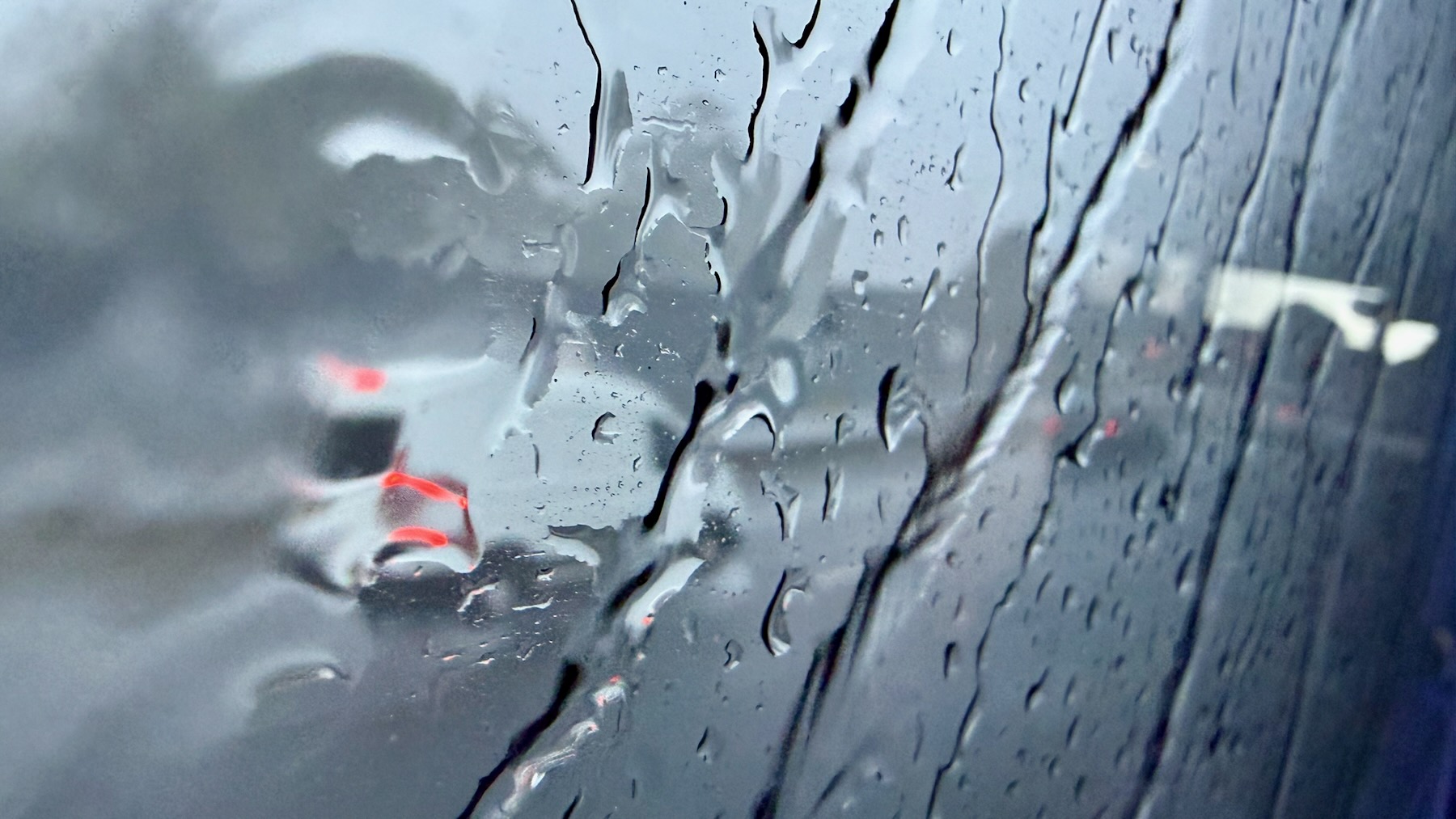 Looking out through the coach window all is wet. Streams of water run down the window. Everything is grey and blurry. A white van can just be made out, its shape rippled and distorted.