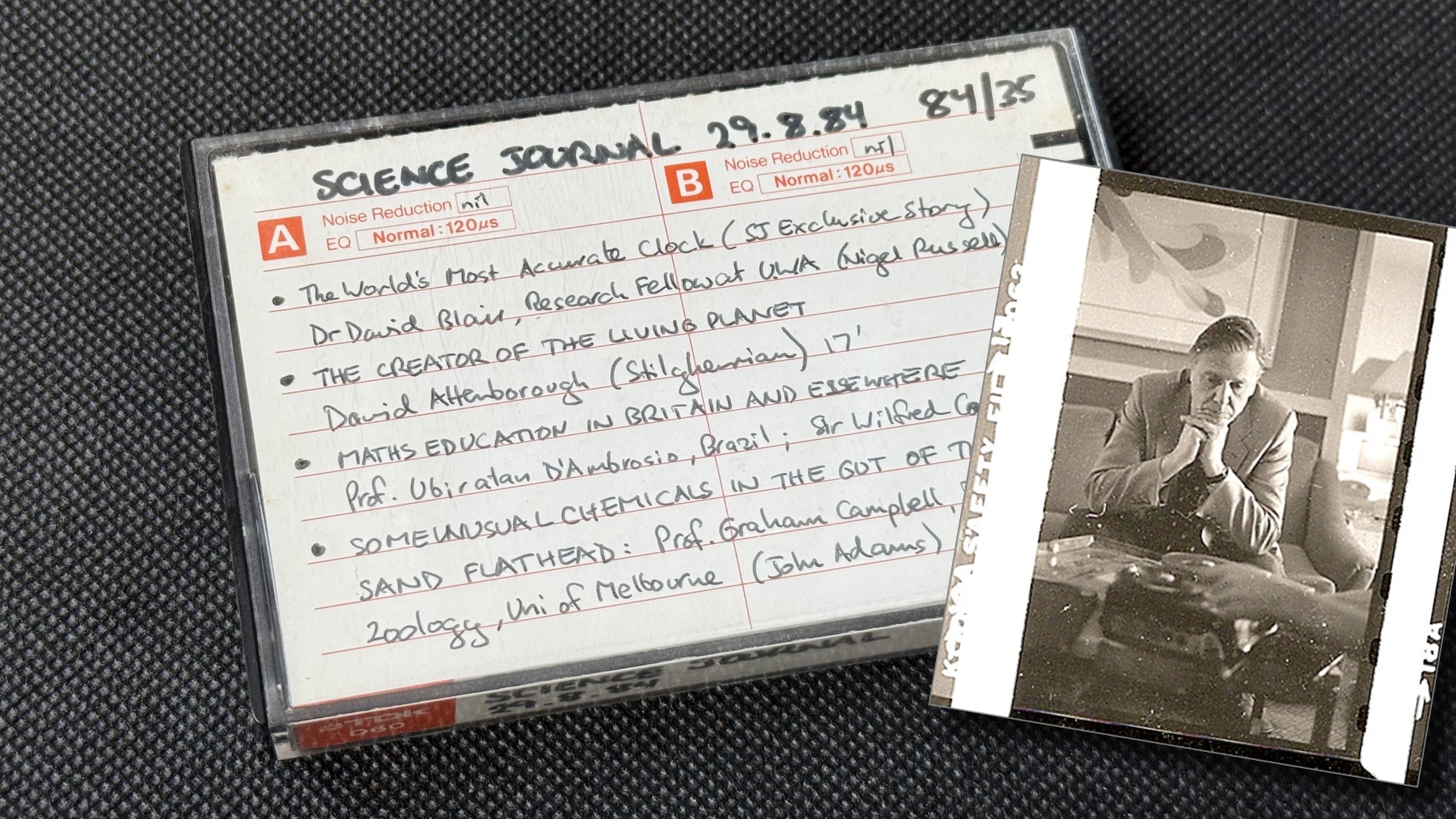 Photograph of an audio cassette in its plastic case. A handwritten insert reads “Science journal 29.8.84 84/35” and then a list of the program items. (See later on the web page.) On the right-hand side is a the scan of a scratched-up black and white photo, with 35mm film sprocket holes. It’s a hotel room. A middle-aged white man in a grey suit sits on the couch with his elbows on the coffee table. He looks very tired. In the foreground, out of focus, the hands of someone off-camera load a reel of quarter-inch tape onto a Nagra recorder. Conversation is imminent.