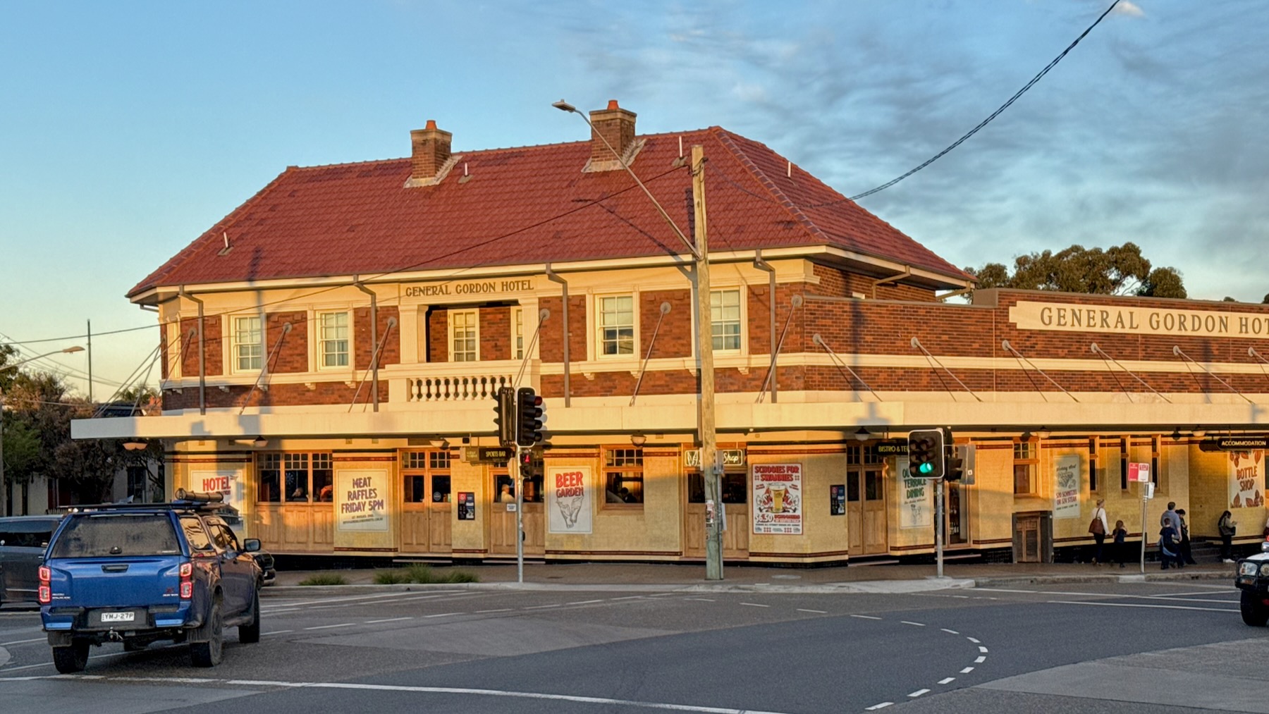 A Sydney suburban pub lit by the late afternoon sun. The ground floor is tiled in yellow. The upper floor is red brick with matching yellow trim around the windows and elsewhere. The roof is red tiles. The sign reads: General Gordon Hotel.